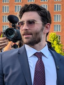 By Poisonwithahawkseye - Own work, CC BY 4.0, https://commons.wikimedia.org/w/index.php?curid=190993358 Hasan Piker speaking at an outdoor event